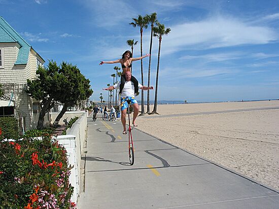 Julie sitting on Eric's shoulders, while he rides his unicycle down the strand, Balboa Peninsula, Newport Beach, California